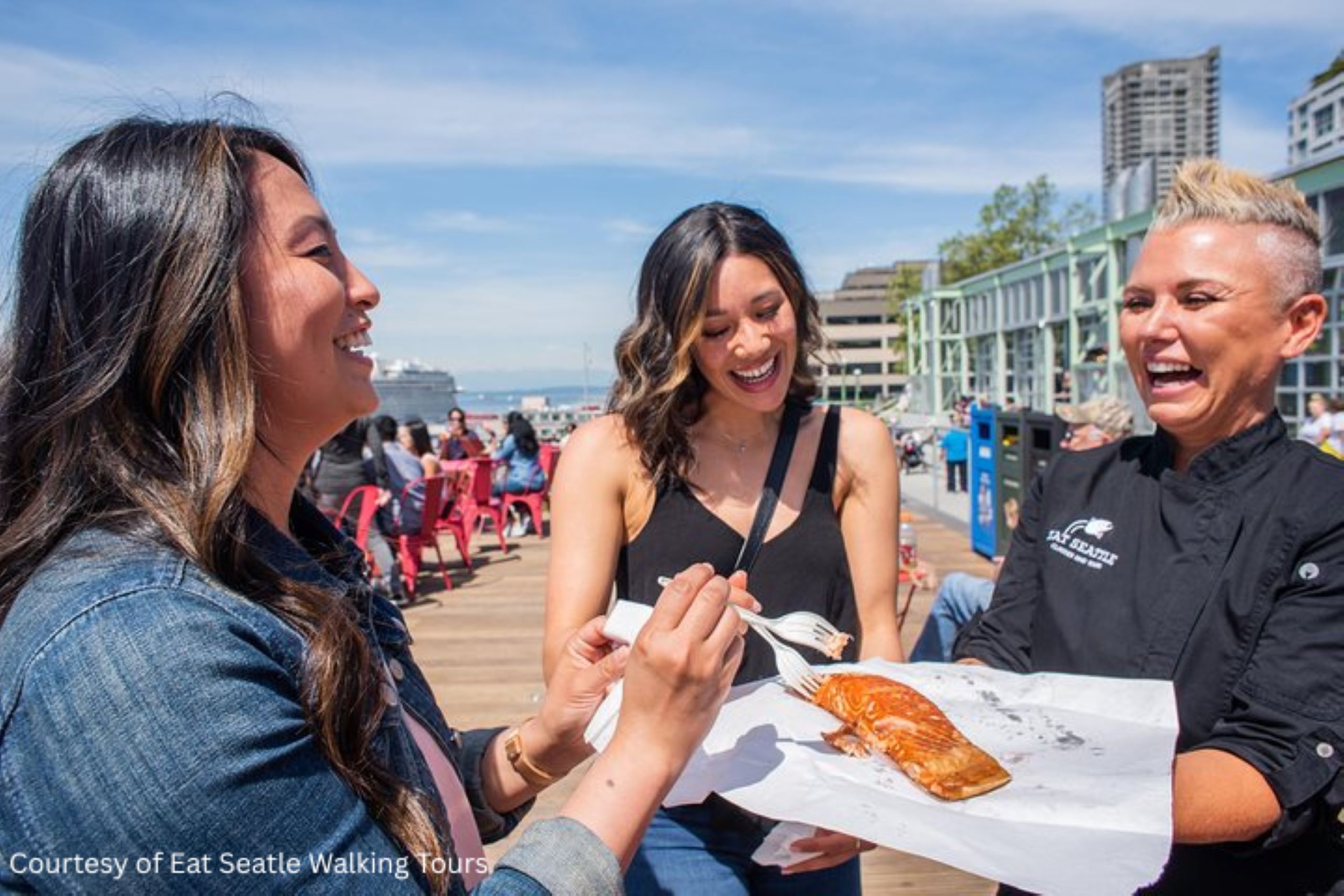 Three women enjoying a fresh seafood tasting on the Eat Seattle Walking Tour along Seattle’s waterfront.