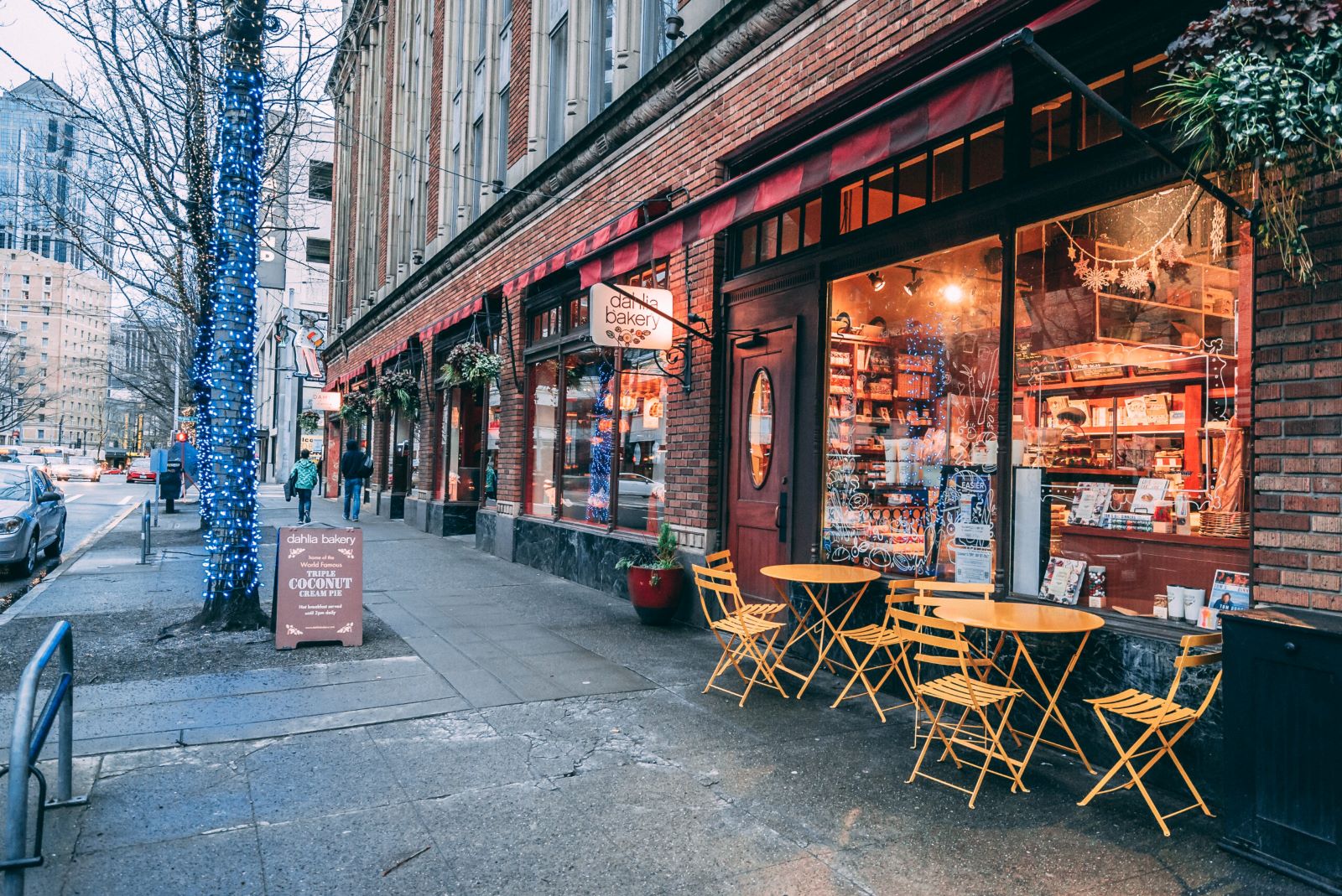 Exterior of Dahlia Bakery in downtown Seattle with yellow café tables and festive lights