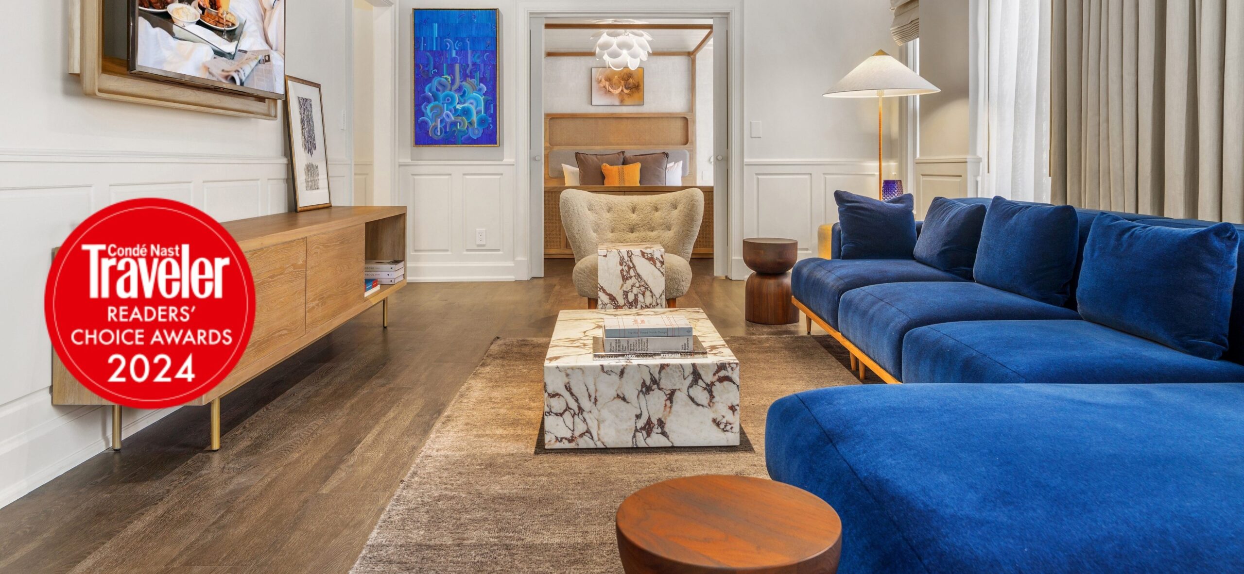 Hotel Ändra Seattle suite living room with blue velvet sofa, marble coffee table, and Condé Nast Traveler Readers' Choice Awards 2024 badge