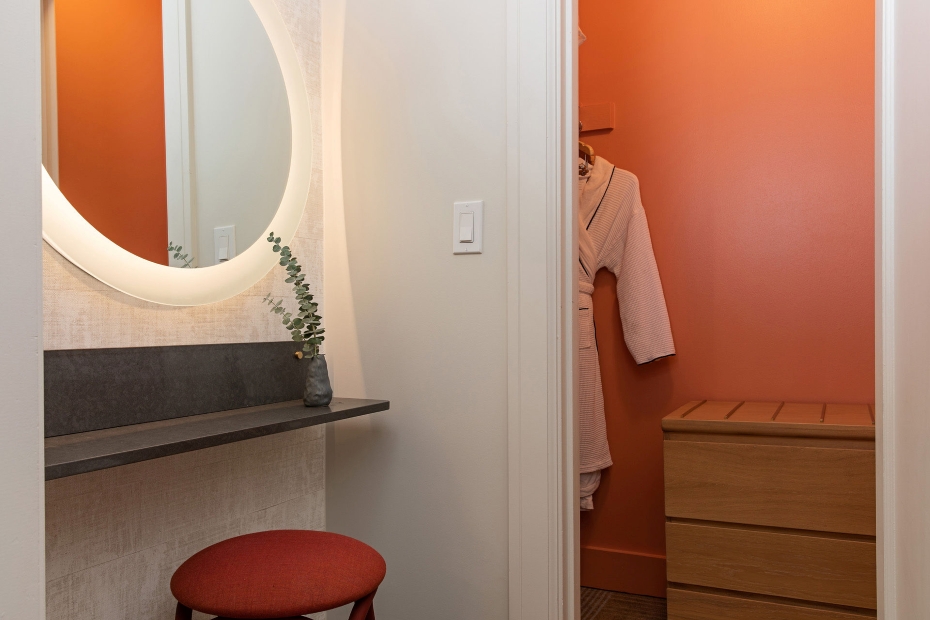 Junior Suite dressing nook with backlit round mirror, vanity, and coral closet with robe at Hotel Ändra Seattle